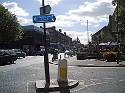 A church building on the left and shopping centre on the right. In the middle a busy road.