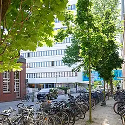 View of the main administration building and the mensa area. Many bicycles are parked in front of the buildings.