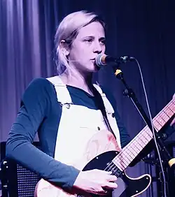 Deland playing guitar and singing into a microphone