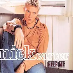 An image of a man wearing an orange dress shirt and blue jeans, sitting down with his right arm on his right knee.