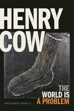 A photograph of a woven sock with "HENRY COW" in large type in the top left, "THE WORLD IS A PROBLEM" in smaller type in the bottom right, and "BENJAMIN PIEKUT" in small text in the bottom left
