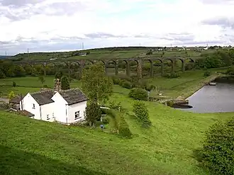 A white cottage in the foreground, a dam head and water in the middle ground, and a railway viaduct in the background