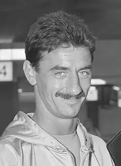 Black and white photo of Ian Rush. He has a moustache and is wearing a light coloured tracksuit. He is looking directly at the camera while smiling