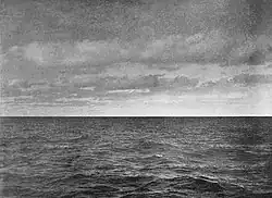 A black and white photograph of the ocean without waves. A white glow, the iceblink, fills the sky.