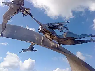 Shiny steel sculpture of woman gliding over a wave along with two seagulls