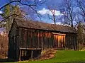 An unpainted wooden barn with a shingle roof in the sunlight