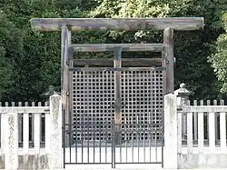 Wooden torii gate and concrete fence in front of trees.