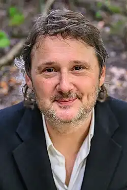 close-up image of Joost Zweegers wearing a white shirt and dark blue blazer, smiling directly at camera