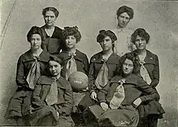Black-and-white team photo of the 1903 KU women's basketball team with the center-most girl holding a basketball with "1903" painted on it