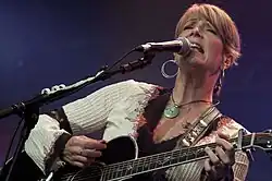 Country music singer Kathy Mattea singing into a microphone while strumming a guitar.
