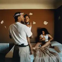 In a bedroom, Kendrick Lamar wearing a diamond encrusted crown of thorns is seen holding his daughter with his wife seen sitting on a bed holding his son. The bedroom has brown paint with white spots and a radiator.
