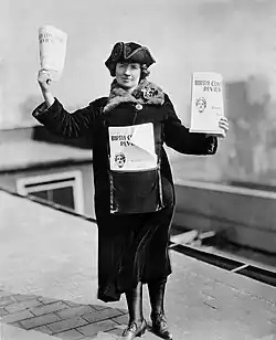 A woman standing on a street, holding flyers for sale.
