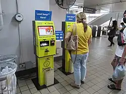 A woman uses a bright yellow machine to reload her Beep card at a train station.