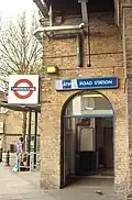 A beige-bricked building with a dark-blue, rectangular sign reading "LATIMER ROAD STATION" in white letters all under a white sky