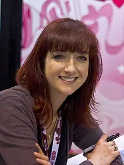 Photo of a smiling woman with medium length red hair and a purple shirt.