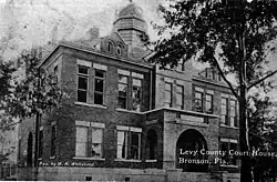 A black and white photograph of a large brick building with two stories and a small dome