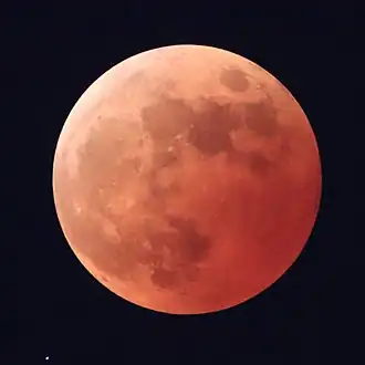 A mostly dark-red colored Moon