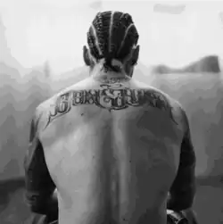 The cover is a black and white photo of Maluma facing away from the camera, sitting down with no shirt on and showing the tattoo on his back