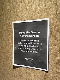 A paper poster on the wall that reads: "Save the drama for the screen: Loud or disruptive behaviour will result in being asked to leave — and nobody wants to miss the ending."