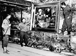 Black and white photograph of members of the MFAA looking at a large painting found in a German salt mine