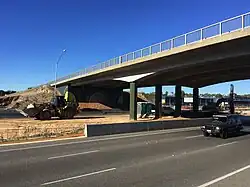 A concrete bridge over a highway with construction vehicles within the highway median strip
