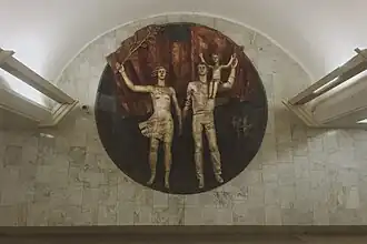 A statue of a man and woman holding hands. A boy sits on the man's shoulder. The sculpture is set into the wall, inside a circle.