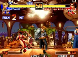 A 2D screenshot of a fighting match between two player characters. A blonde woman in a long black skirt with a slit and a white vest kicks a brown haired woman in a red sleeveless uwagi with an extended loincloth and a decorative sash. Two yellow meter bars signifying character health percentage are at the top of the screen with a timer between them.