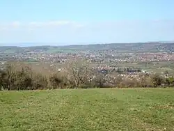 lots of house roofs, with trees and grass in the foreground and hills in the distance.