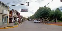View down a street with shops on one the left and a tree-lined park on the right