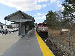 A diesel locomotive leading a passenger train into a suburban station with a curved high-level platform
