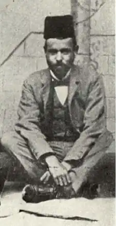 Photograph of a young man with a short beard, seated, wearing a Turkish fez.