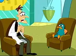 A cartoon Caucasian man wearing a white lab coat sits on a brown coach with a sad and sincere look on his face. Across from him is a green platypus bearing the same expression and on the same kind of couch. Behind them is a TV set with blue walls and a large yellow sign.