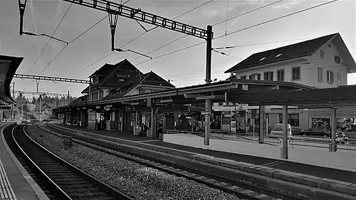Three-story hip-roofed building next to double-track railway line with canopy-covered side platforms