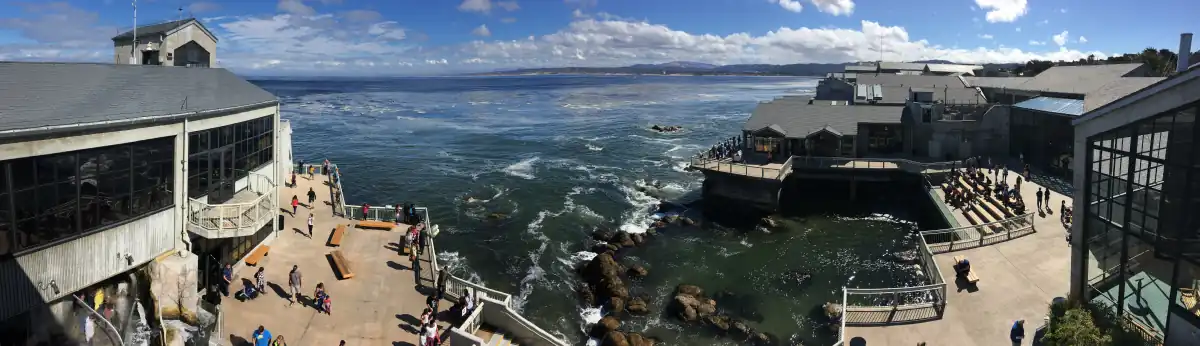 Panoramic view of the aquarium's 20,000 square feet (1,900 m2) of public decks overlooking Monterey Bay. The building's walls on either side consist mostly of windows, but there is stadium seating to the right overlooking a man-made tide pool