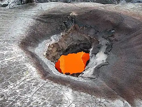Large hole in the ground revealing an underground tunnel carrying a river of lava