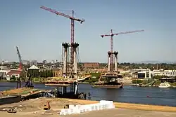 A cable-stayed bridge with the deck partially built and a construction crane atop each of the two pylons