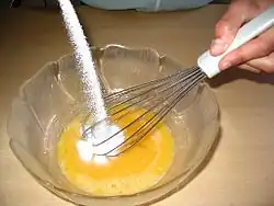 Bowl with eggs. White sugar is being poured in.