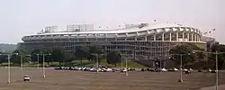 A large circular stadium with a curving overhang behind a mostly empty parking lot.