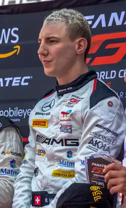 Raffaele Marciello sporting racing overalls and standing on the top step of an outdoor podium