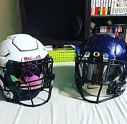 Two Riddell football helmets, on the left is a white Speedflex, on the right is a blue Speed.