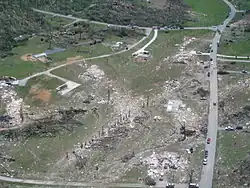 Ground scouring and homes are destroyed along a rural road.