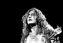 A black and white photograph showing a headshot of Robert Plant with a microphone in hand