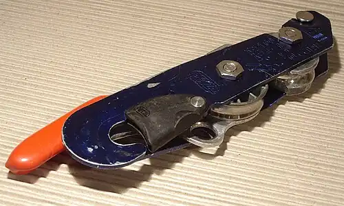 A bobbin type descender covered blue, with a plastic covered handle on the left side of the device