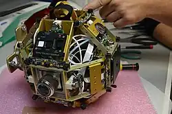 A SPHERES satellite without the plastic shell. Aluminum structure, a control panel, ultrasonic sensors, thrusters, pressure regulator knob and pressure gauge are visible.