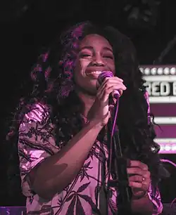 SZA smiling while speaking to a microphone