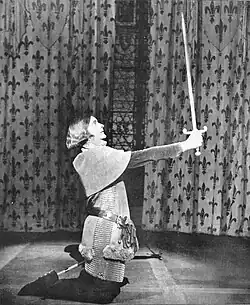 Young white woman in men's military armour, kneeling and brandishing a sword