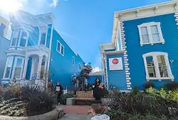 Two buildings, blue with white trim, on a sunny day. They are separated by a courtyard. The right building bears a sign with the name and logo of the Community Music Center.