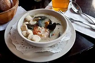 A cream-style seafood chowder at a restaurant, served with oyster crackers in the bowl at left