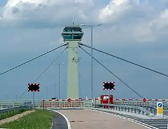 A cable-stayed tower with barriers and flashing lights on the road deck beneath