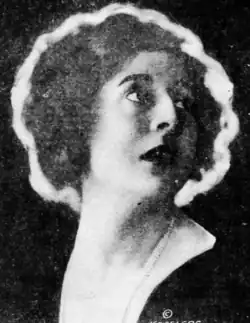 A white woman with bobbed wavy hair, looking back over one shoulder